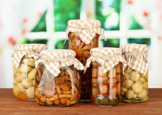 Delicious marinated mushrooms in glass jars on wooden table on bright background