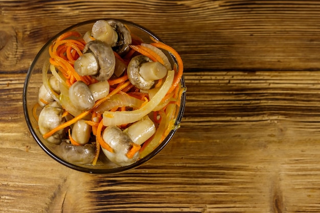 Delicious marinated mushrooms with carrot onion and spices in glass bowl on wooden table Top view