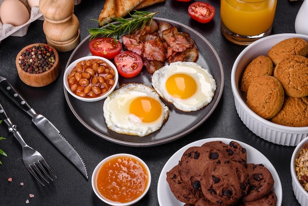 A delicious nutritious healthy breakfast with fried eggs bacon beans a glass of juice oat cookies milk and jam Healthy eating at the beginning of the day