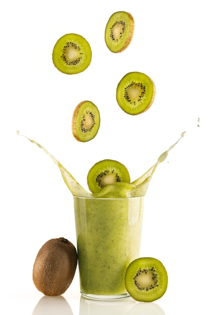 Delicious and nutritious slices of kiwi falling into a glass of fresh kiwi smoothie on white background. Nutritious natural drink for a healthy lifestyle. Organic, vitamin and detoxifying drink.