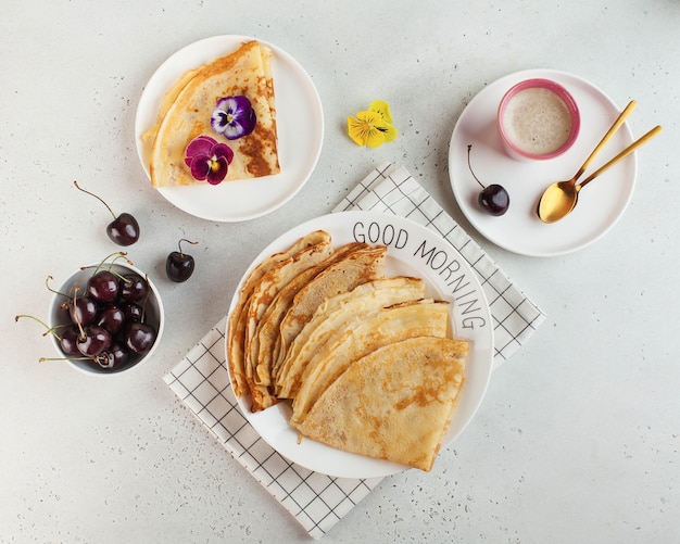 Delicious pancakes on plates, decorated with flowers and berries, coffee mug. Concept of Breakfast, good morning.