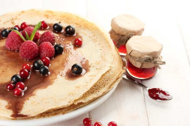 Delicious pancakes with berries and jam on plate on wooden table