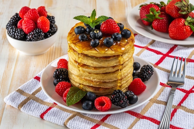 Delicious pancakes with fresh berries on white wooden table 