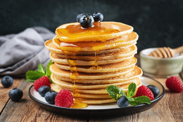 Delicious pancakes with fresh blueberries raspberry and maple syrup or honey on a dark background