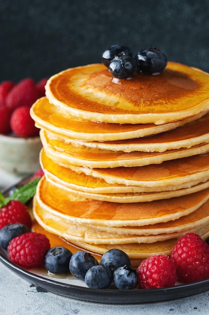 Delicious pancakes with fresh blueberries raspberry and maple syrup or honey on a dark background