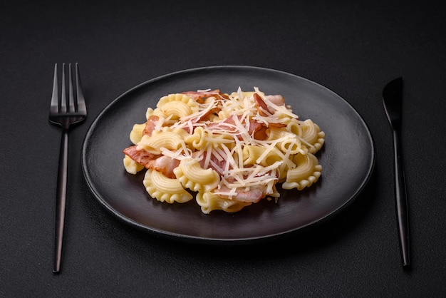 Delicious pasta with bacon and parmesan cheese on a black ceramic plate