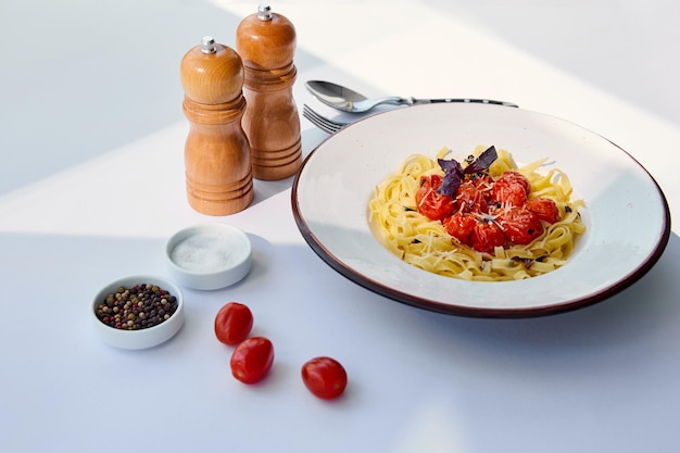 delicious pasta with tomatoes served with cutlery salt and pepper mills on white table in sunlight