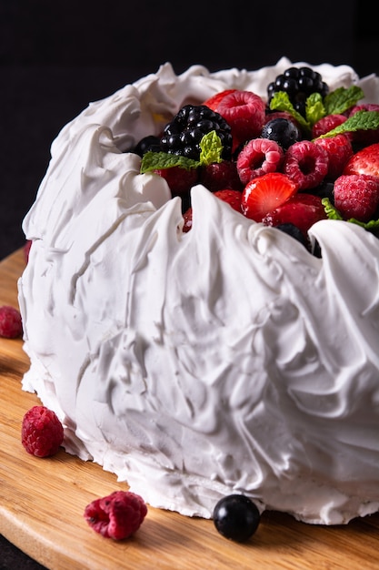 Delicious Pavlova cake with meringue topped and fresh berries on black background