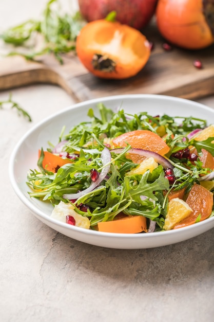 Delicious persimmon salad with arugula  and orange served on light grey table, flat lay. Space for text