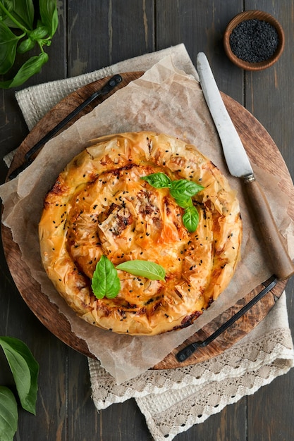 Delicious pie Spanakopita with soft feta cheese and spinach on old dark wooden table backgrounds Traditional Greek Spiral filo pastry pie spanakopita in shape of roll Traditional Greek cuisine