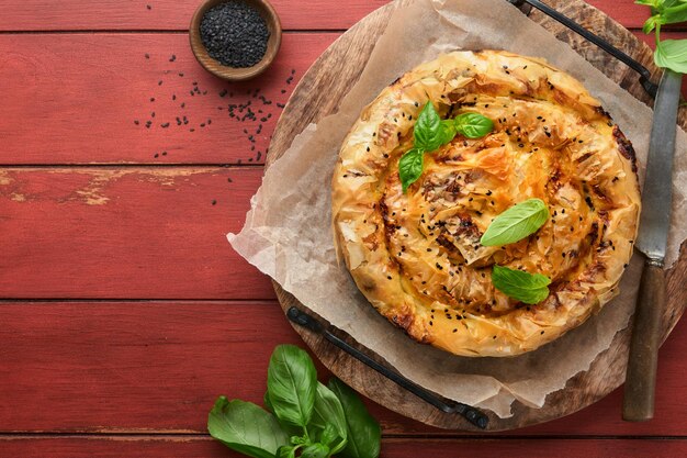 Delicious pie Spanakopita with soft feta cheese and spinach on old red wooden table backgrounds Traditional Greek Spiral filo pastry pie spanakopita in shape of roll Traditional Greek cuisine