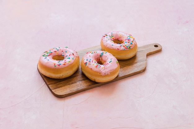 Delicious pink donuts with sprinkles on wooden chopping board