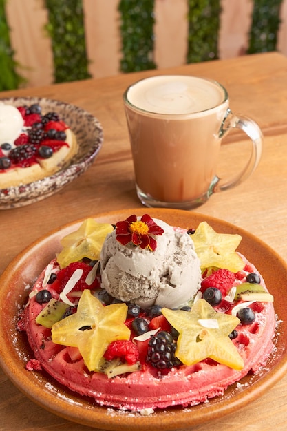 Delicious pink ice cream waffle with red fruits and starfruit on wooden table