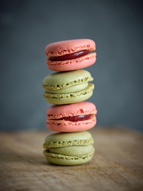 Delicious pistachio and strawberry flavored macaroons with sweet filling stacked on top of each other against gray background in room