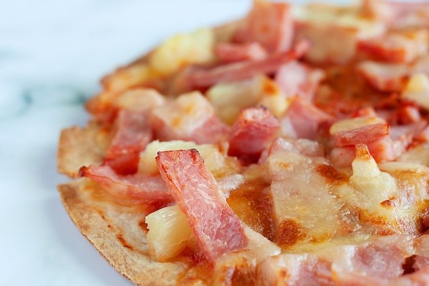 Delicious pizza with pineapple, ham slice, bacon slice, mozzarella cheese, pizza sauce on white marble background