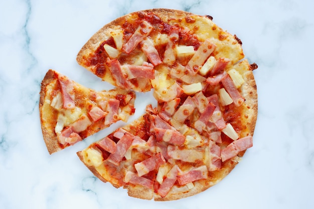 Delicious pizza with pineapple, ham slice, bacon slice, mozzarella cheese, pizza sauce on white marble background