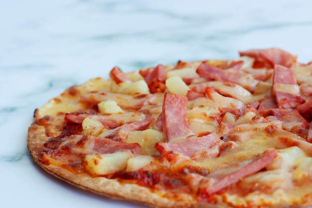 Delicious pizza with pineapple, ham slice, bacon slice, mozzarella cheese, pizza sauce on white marble background