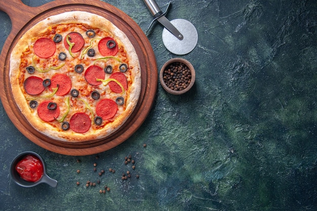 Delicious pizza on wooden cutting board and pepper ketchup on isolated dark surface