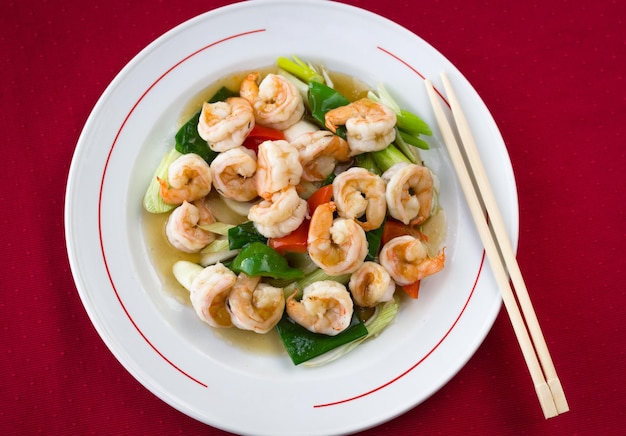 Delicious plate of king prawns with green and red bell peppers, onion pieces and chopsticks