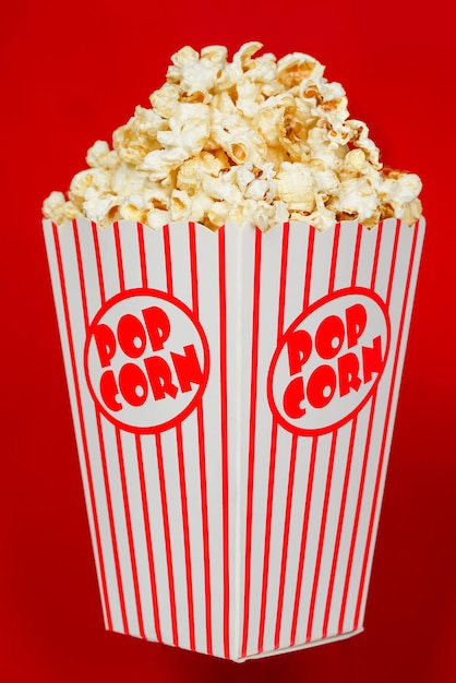 Delicious popcorn in a red striped paper cup on a red backgroundSelective focus