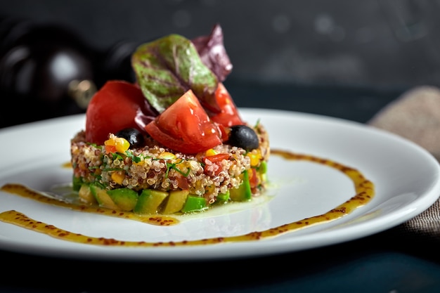 Delicious quinoa salad with avocado and tomatoes on black background.