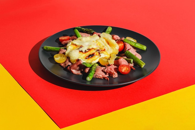 Delicious raclette cheese served over roast beef with tomatoes and asparagus dish on red background