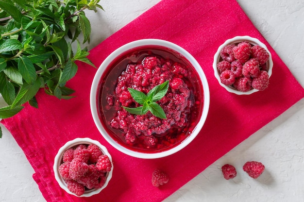 Delicious raspberry jam in a bowl fresh berries mint leaves on a pink napkin Top view