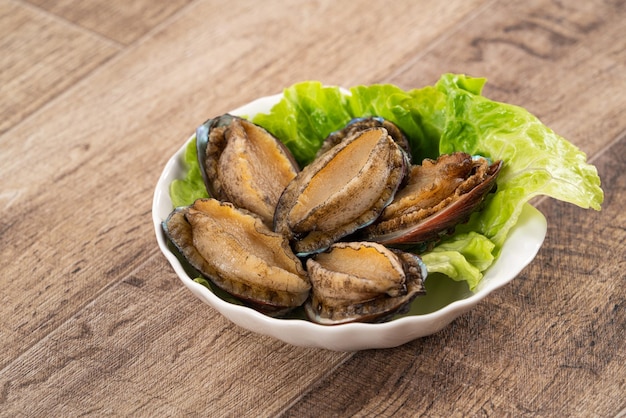 Delicious raw abalone in a plate on wooden table background