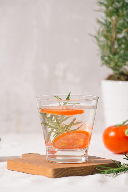 Delicious refreshing water with rosemary and tomato in glass on table