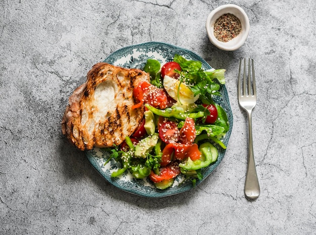 Delicious salad for breakfast snack salad with salmon egg vegetables lettuce and grilled bread on a grey background top view