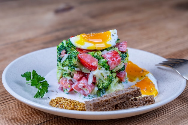 Delicious salad with broccoli, tomato, onion and boiled egg with cream sauce in a plate on wooden background. Healthy food, close up