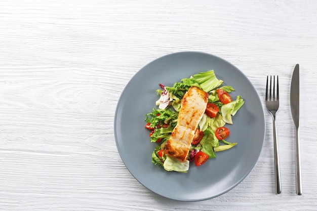 Delicious salmon with salad and flatware on wooden table