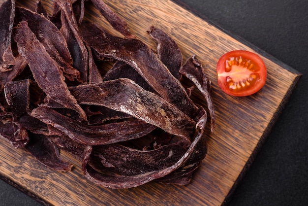 Delicious salted dried beef cut into slices as an appetizer for beer on a dark concrete background