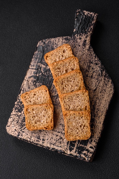 Photo delicious salted rectangular wheat croutons with salt and spices on a dark concrete background