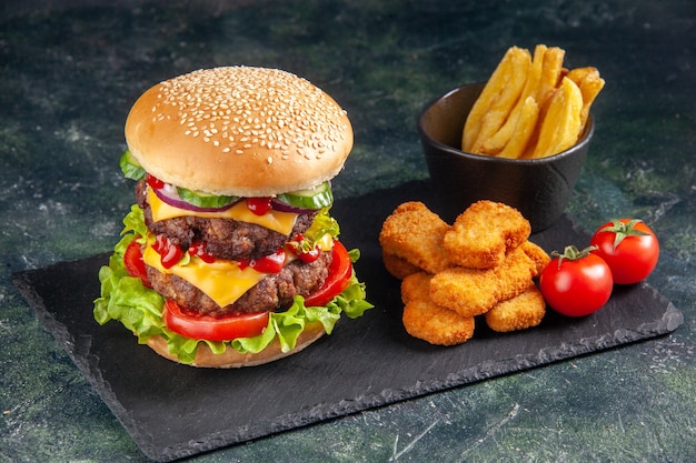 Delicious sandwich on dark color tray and chicken nuggets tomatoes fries on black surface