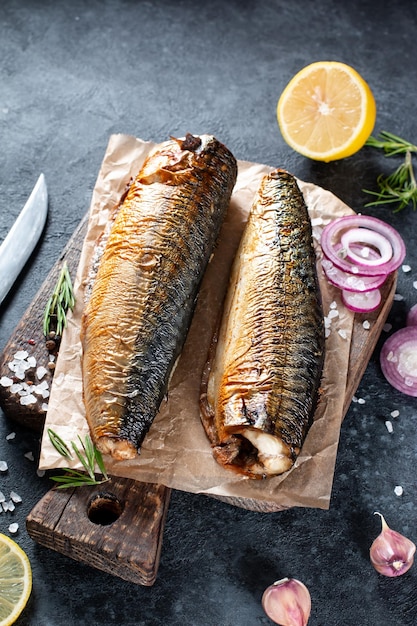 Delicious smoked fish mackerel on paper with garlic and onion rings On rustic background