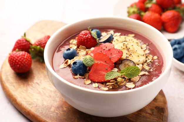 Delicious smoothie bowl with fresh berries banana and granola on table closeup