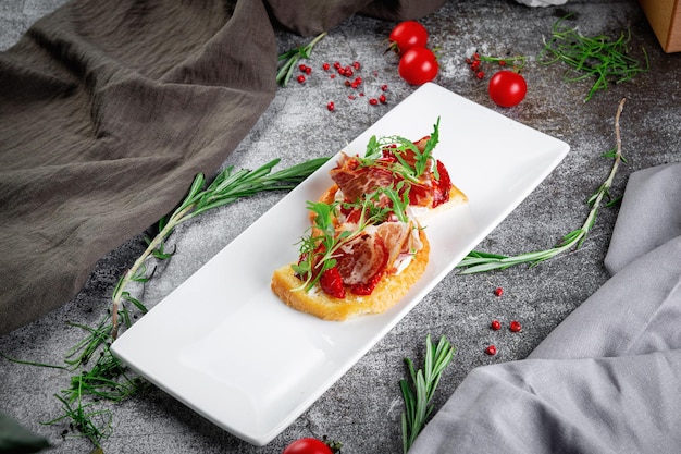 Delicious snacks Bruschetta with bacon roasted tomato red onion rings and arugula Toasted croutons with dried meat and lettuce