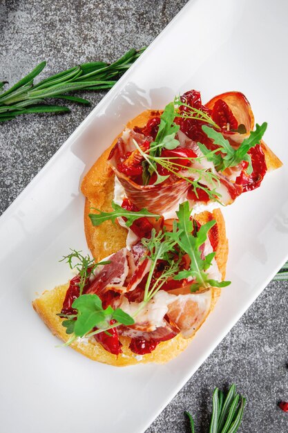 Delicious snacks Bruschetta with bacon roasted tomato red onion rings and arugula Toasted croutons with dried meat and lettuce