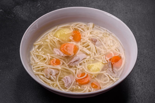 Delicious soup with noodles chicken and carrots with spices and herbs on a dark concrete background