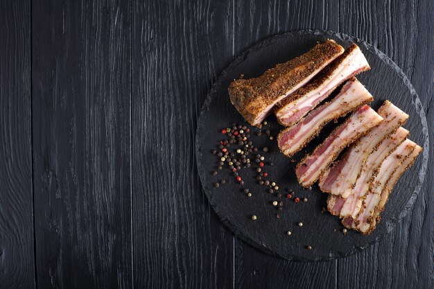 Delicious spiced smoked speck cut in slices on black slate plate