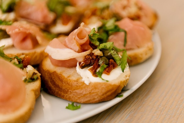 Delicious spicy tomato Italian snacks or bruschetta on slices of toasted baguette decorated with basil red fish ham on a wooden board