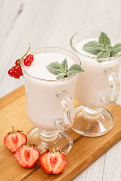 Delicious strawberry yogurt with mint leaves in glasses and fresh cut strawberries on wooden cutting board