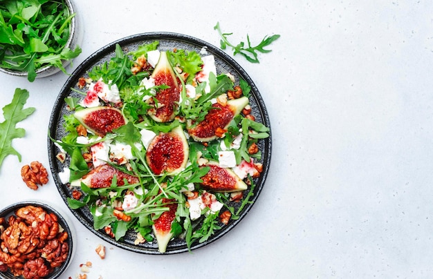 Delicious summer salad with sweet figs white feta cheese walnuts arugula and jam vinegar dressing on white table background top view negative space