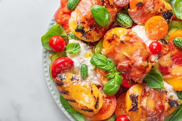 Delicious summer warm salad with grilled peaches vegetables and cheese on white background Close up