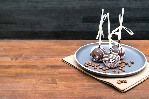 Delicious sweet chocolate cake pops popsicles decorated white sprinkles on plate wooden background pastry desserts on stick with tape Tasty food mock up template copy space