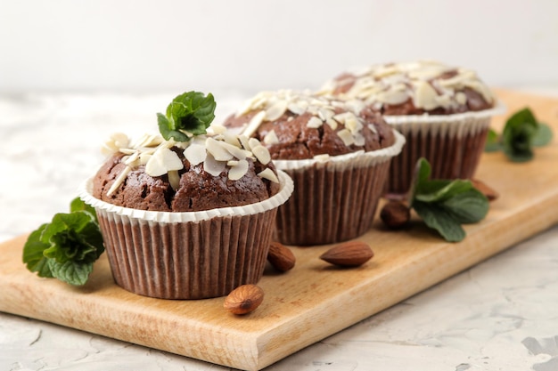 Delicious, sweet chocolate muffins, with almond petals next to mint and almond nuts on a light concrete table. close-up