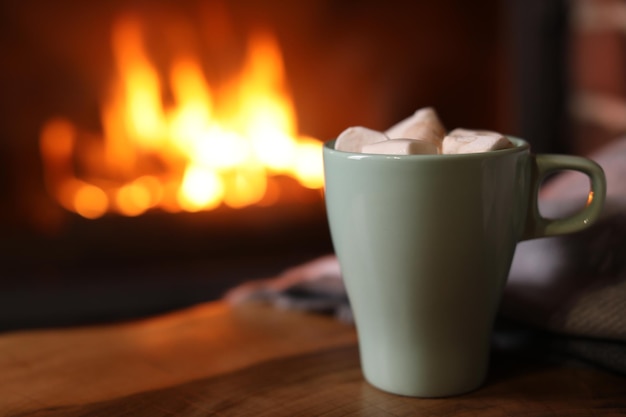 Delicious sweet cocoa with marshmallows and blurred fireplace on background