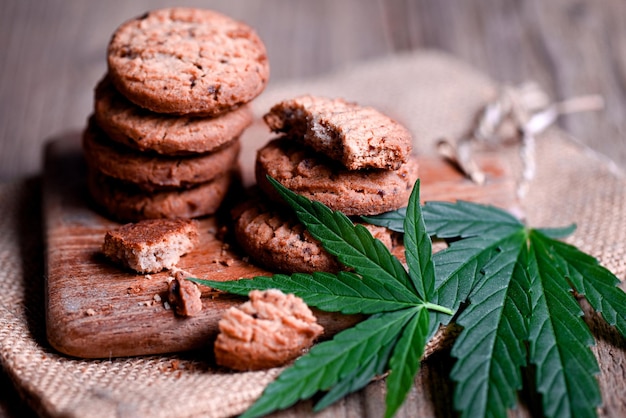 Delicious sweet dessert cookie with hemp leaf plant THC CBD herbs food snack and medical Cannabis food cookies with cake chocolate cannabis leaf marijuana herb on wooden background