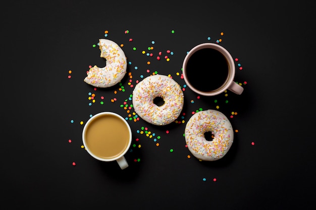 Delicious, sweet, fresh donuts, multicolored decorative candy, a cup of coffee on a black background. Concept of breakfast, fast food, coffee shop, bakery. Flat lay, top view.